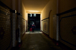 Lächelnder Flink Lieferant steht nachts mit seinem E-Bike und pinker Liefertasche vor einem beleuchteten Gebäude. 