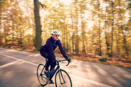 Rennradfahrer fährt auf einer Straße durch den Grunewald – dynamische Szene mit herbstlicher Natur. 