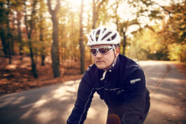 Rennradfahrer fährt auf einer Straße durch den Grunewald – dynamische Szene mit herbstlicher Natur. 