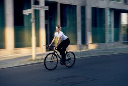 Junge Frau fährt mit einem minimalistischen City-Bike durch eine moderne Berliner Straße. 